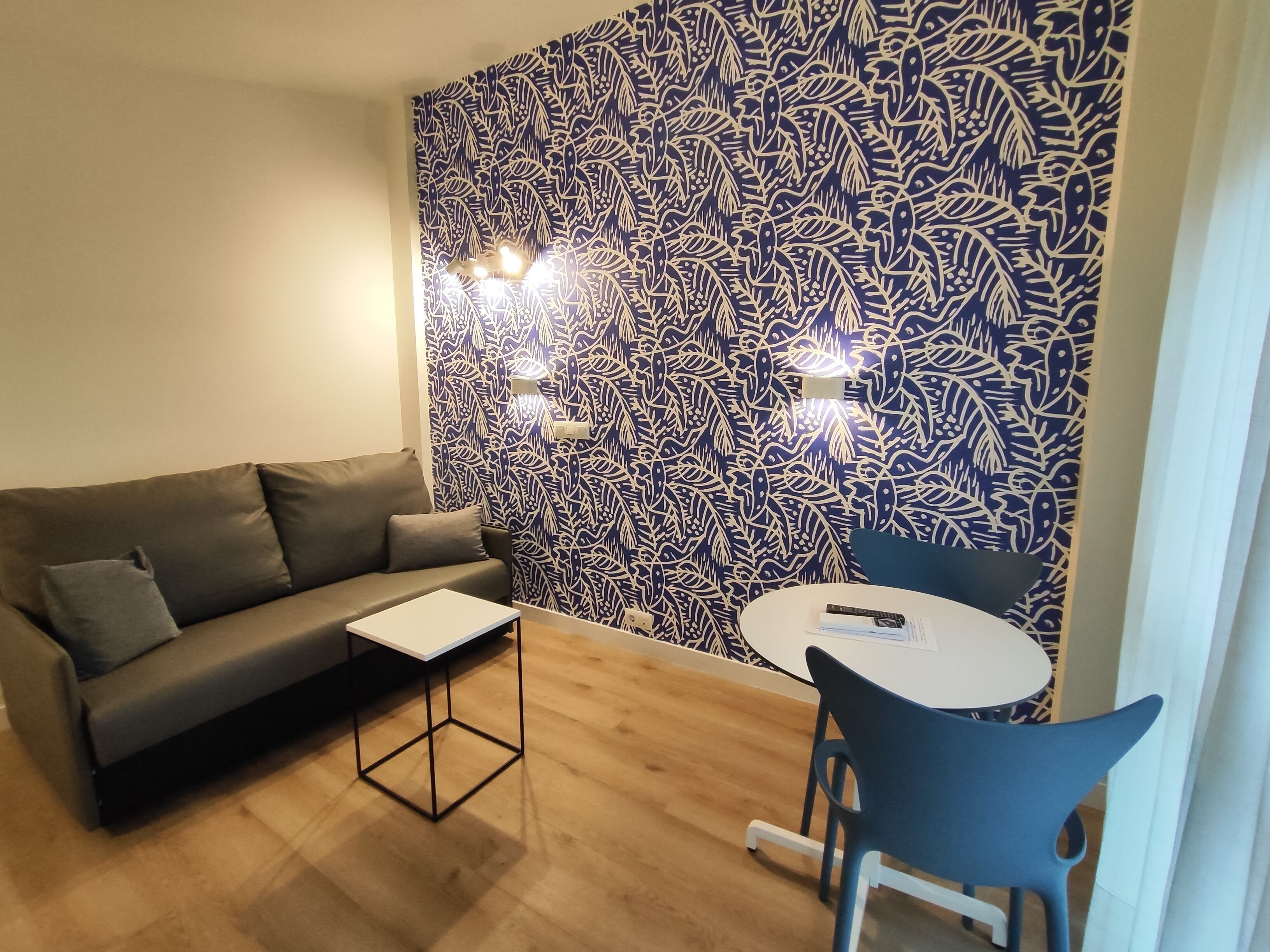 Una sala de estar moderna con una pared estampada, un sofá gris, una mesita y un sillón azul.