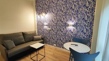 A modern living room with a patterned wall, a grey sofa, a small table, and a blue chair.