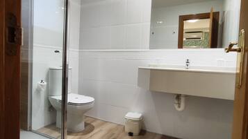Un baño con cabina de ducha de vidrio, inodoro, lavamanos y espejo.