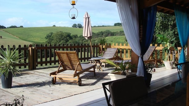 Terraza cubierta al aire libre con mobiliario de madera, cerca de madera y vista a un campo verde.