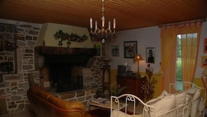 Un salón acogedor con chimenea de piedra, un sofá de cuero, una cama diurna blanca y un cofre de madera.