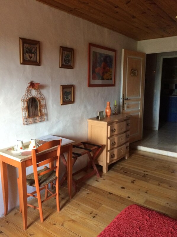 A cozy room with wooden floors, a wooden table with chairs, a dresser, and wall-mounted artwork.