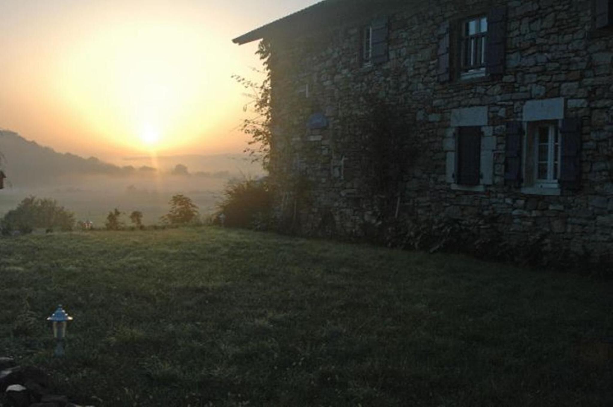A stone building with a grassy yard and a sunrise in the background.