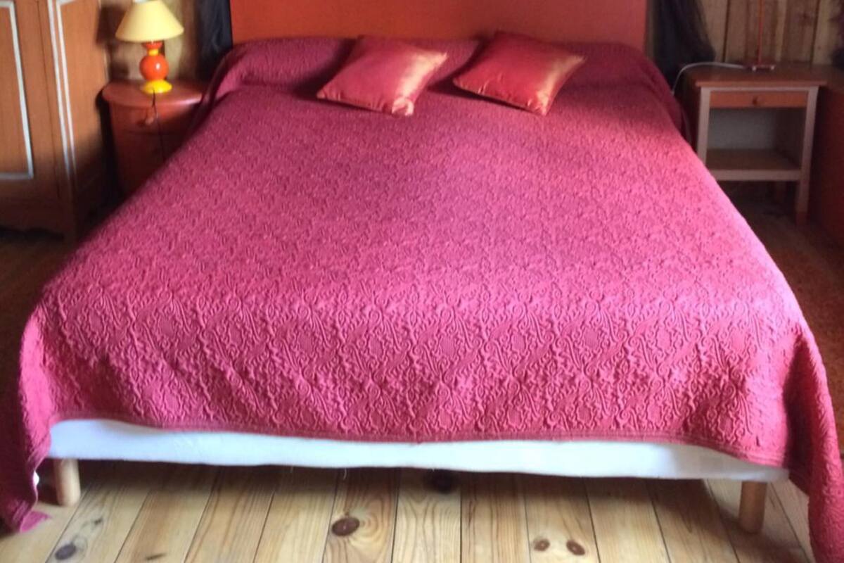 A wooden-paneled room with a bed featuring a red bedspread and matching pillows.
