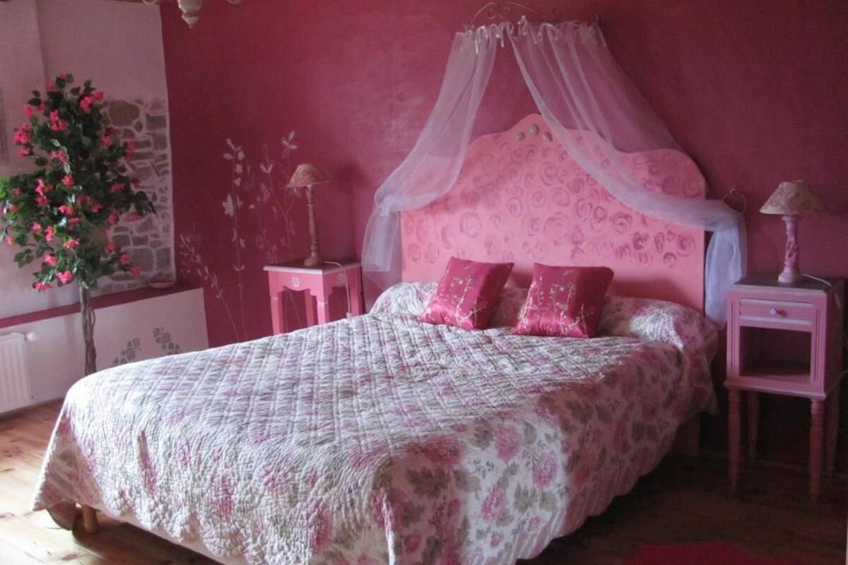 A bedroom with a bed, a nightstand, a lamp, a plant, and a window.