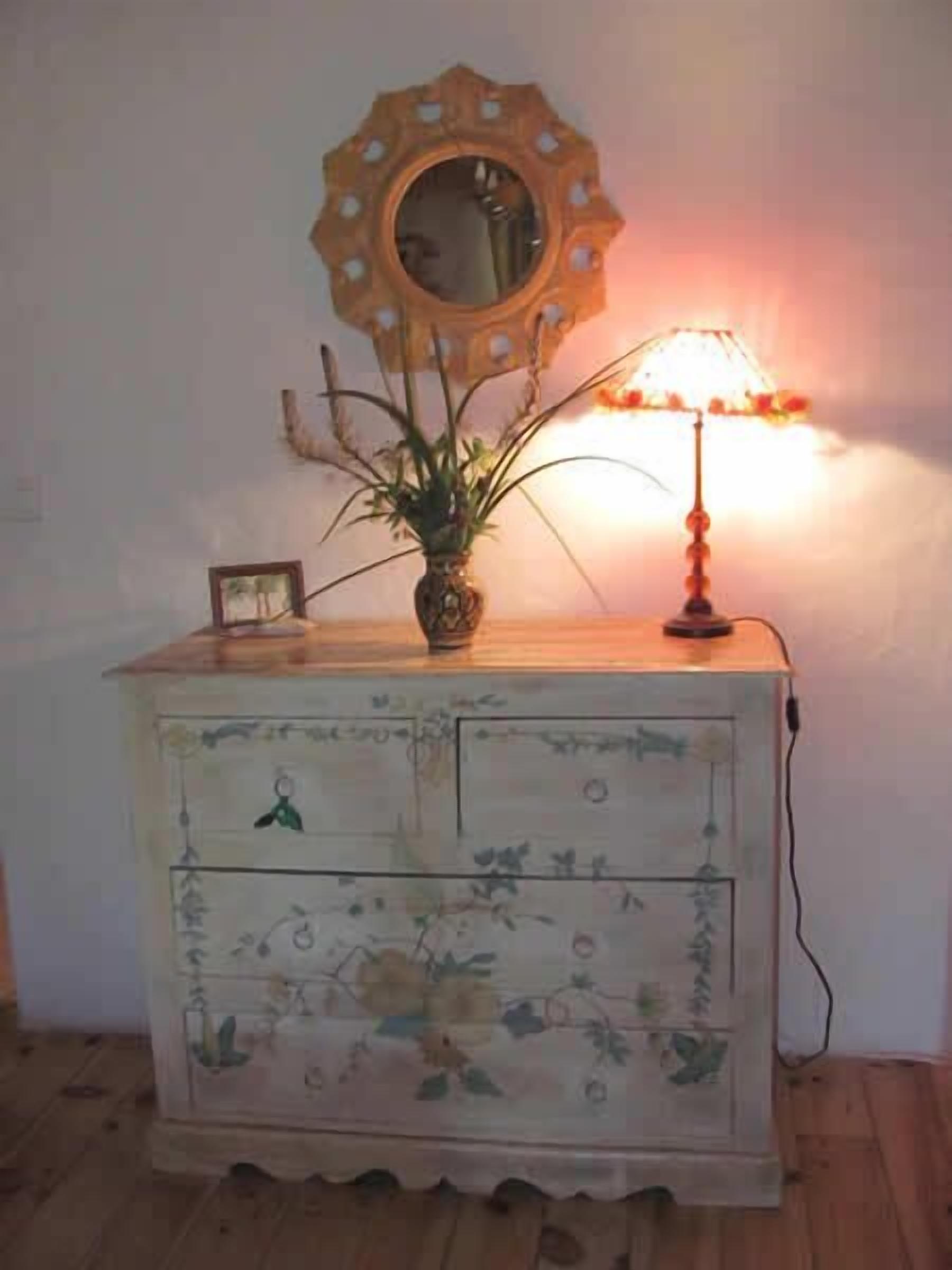Un aparador de madera con motivos florales, un espejo con marco decorativo y una lámpara de mesa.