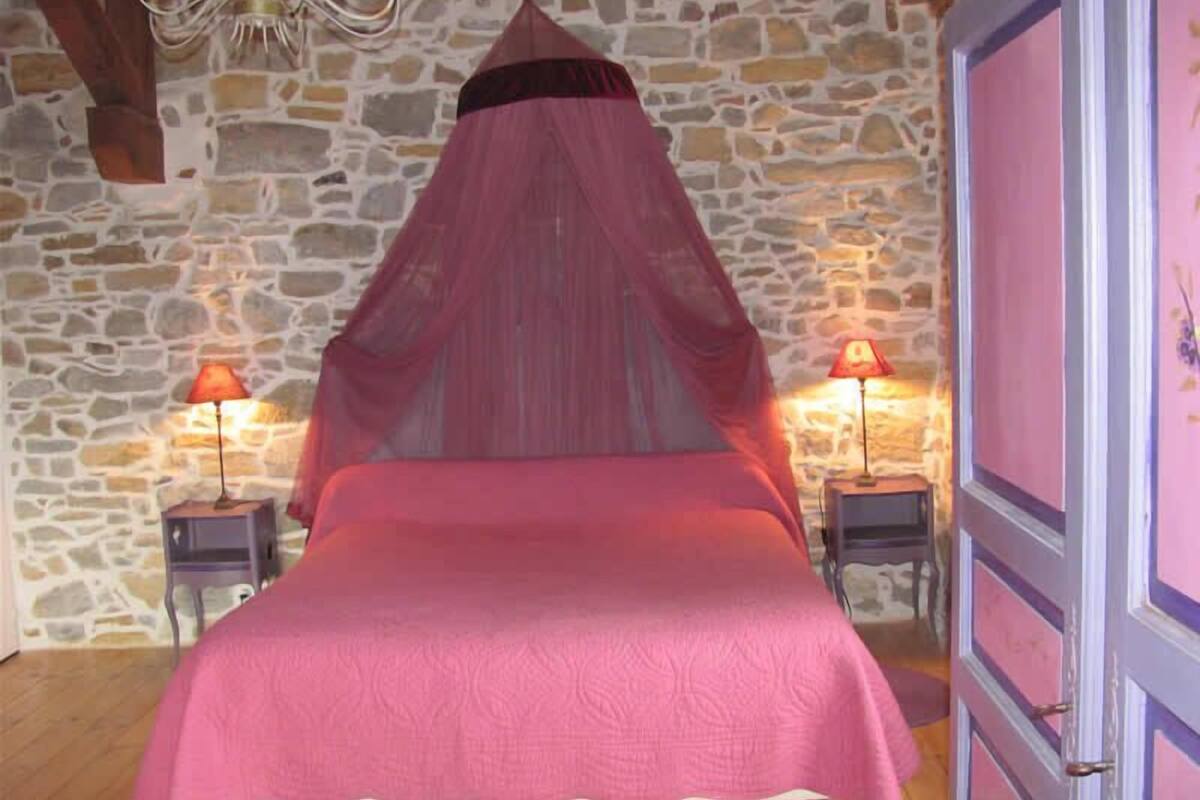 A bed with a canopy in a room with stone walls and two bedside tables with lamps.
