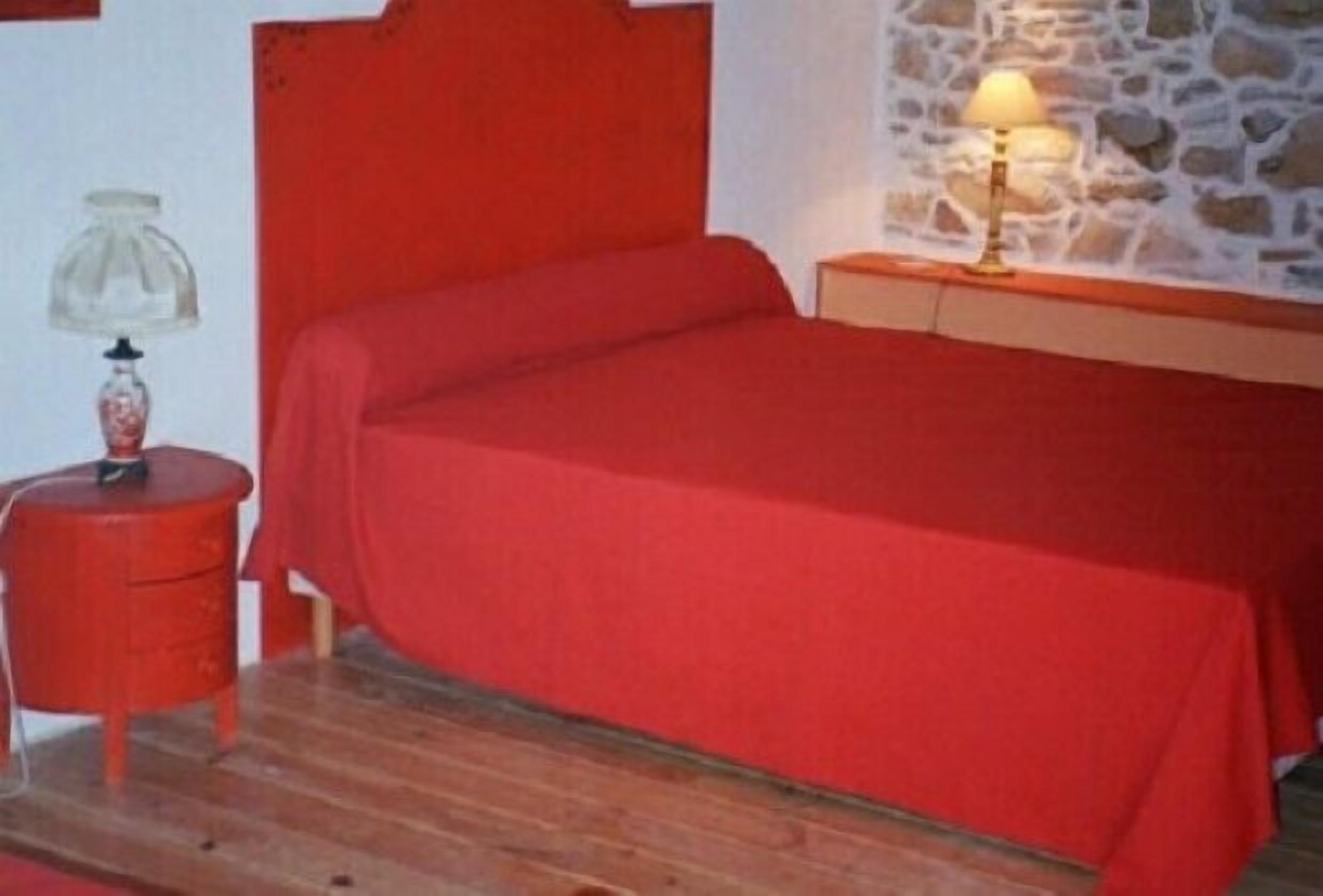 Une pièce avec un lit, une table de chevet, une lampe et un mur en pierre.