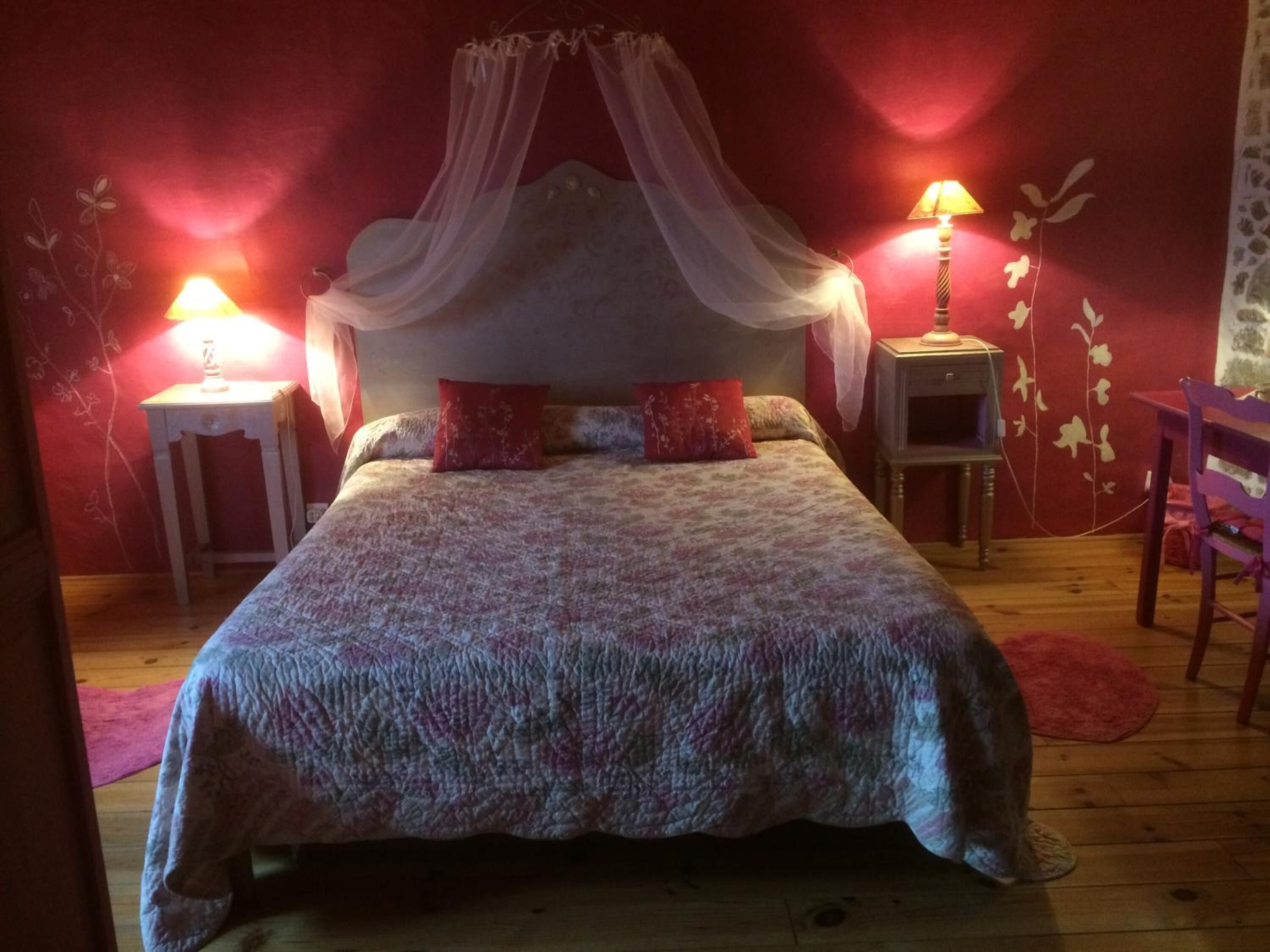 Ein Schlafzimmer mit Himmelbett, zwei Nachttischlampen, einem Sessel und einem kleinen Tisch.