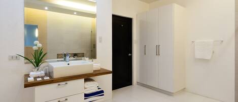 A modern bathroom with a large mirror, white cabinets, and a wooden countertop.