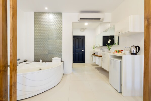 Une salle de bain moderne avec une grande baignoire, une douche, un lavabo et des toilettes. Un miroir est placé au-dessus du lavabo et une porte donne accès à une autre pièce.