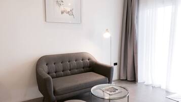 Un salon moderne avec un canapé gris, une table d’appoint en verre, une œuvre d’art encadrée au mur et une lampe sur pied.