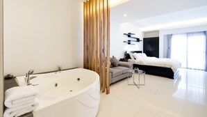 A modern hotel room with a large white bathtub, a sofa, a small table, and a bed with a black headboard. - Winds Boutique Hotel (Angeles City)