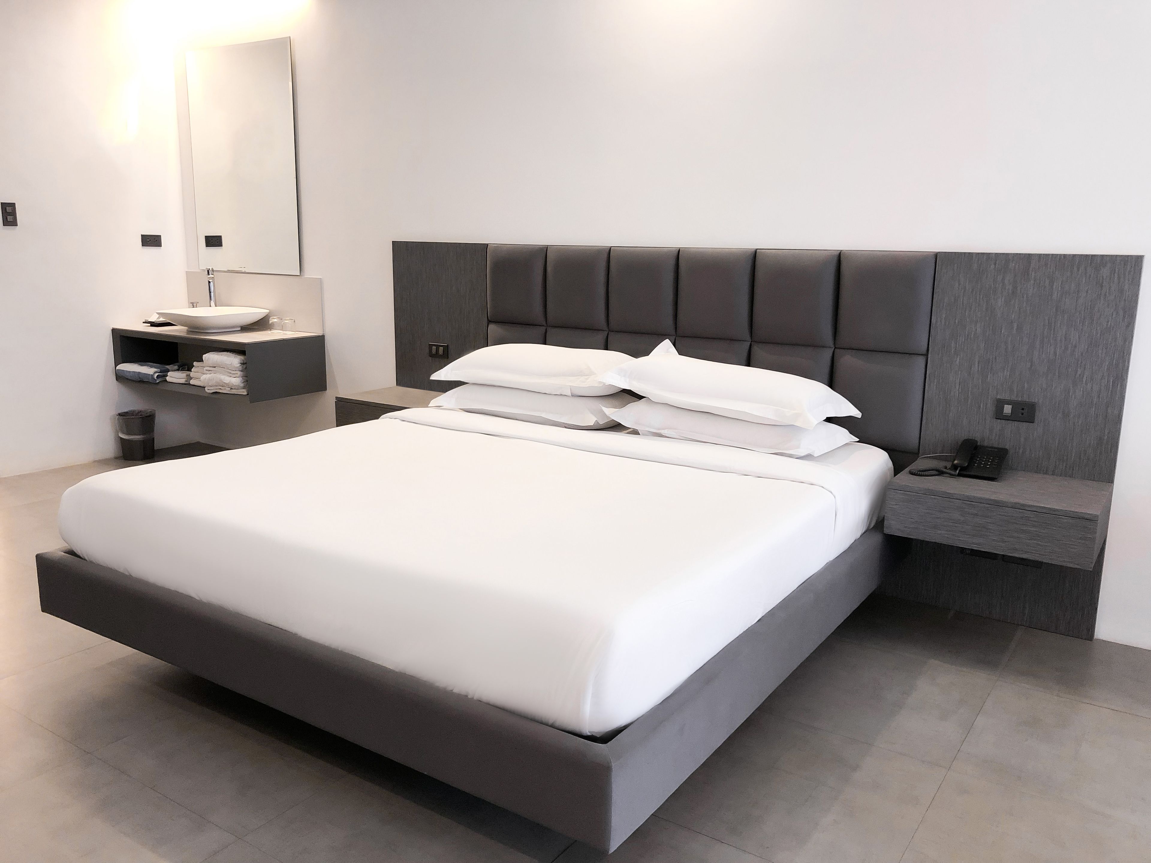 Une chambre d’hôtel moderne avec un grand lit, une table de chevet avec un téléphone et une petite étagère avec des serviettes.
