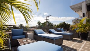 A rooftop terrace with wicker furniture and blue cushions, overlooking a cityscape. - Winds Boutique Hotel (Angeles City)