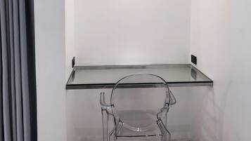 A modern room with a glass desk and a clear chair, a ceiling light, and a grey curtain.