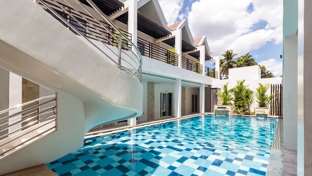 A modern indoor swimming pool with a checkered tile pattern, surrounded by a covered area with a staircase and railings. - Winds Boutique Hotel (Angeles City)