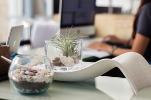 Un bol en verre rempli de sable et de pierres décoratives, un vase en verre contenant une plante et un livre posé sur une table.