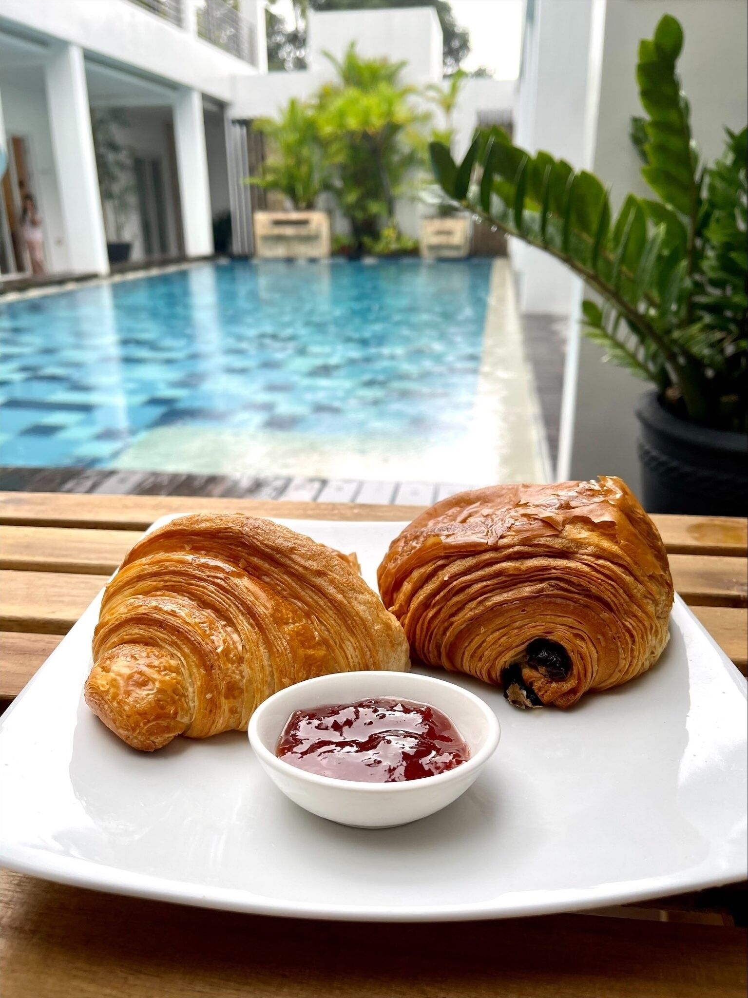 A poolside table with croissants and jam.