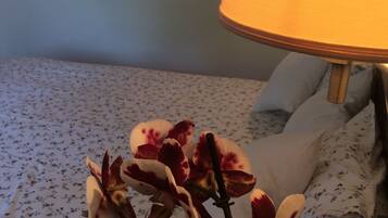 Un lit avec une literie à motifs floraux, une lampe et une plante orchidée.