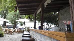 An outdoor seating area with wooden benches and a stone wall backdrop. - Hotel Morfeas (Dio-Olympos)