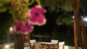 Un área de comedor al aire libre con una mesa y sillas, rodeada de árboles y un muro de piedra.