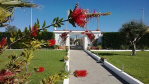 A pathway leading to a building with a white facade and a metal gate. - Lido Impero (Massafra)
