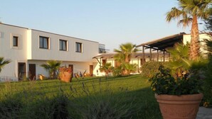 A modern building with a flat roof, multiple windows, and a covered outdoor area with palm trees. - Lido Impero (Massafra)