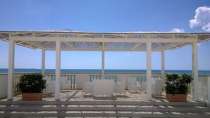 A covered outdoor seating area with white chairs and potted plants, overlooking the sea. - Lido Impero (Massafra)