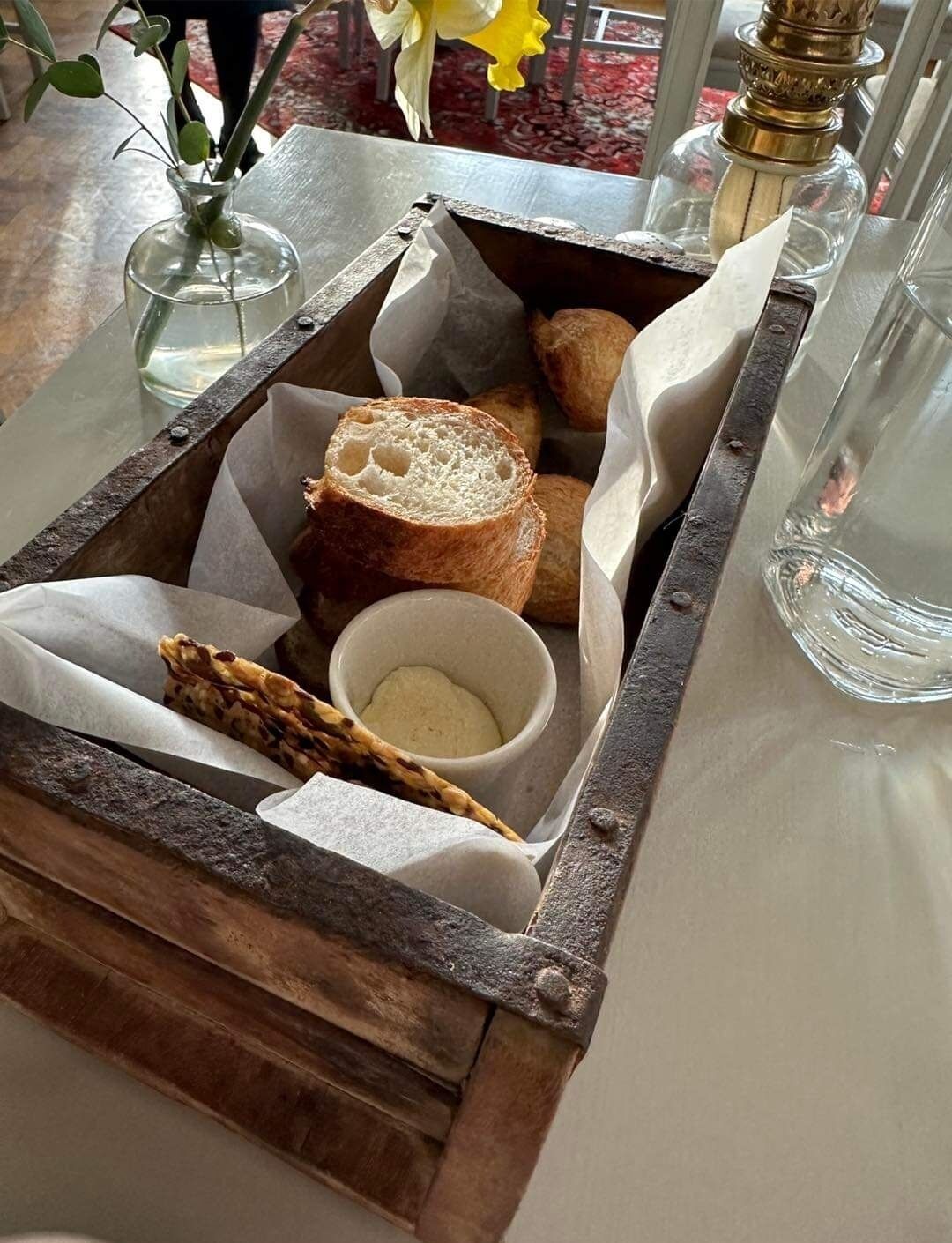 Ein Tablett mit Brot, eine Schale Butter und eine Vase mit Blumen auf einem Tisch.
