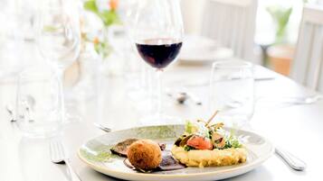 Una mesa de comedor dispuesta con un plato de comida, una copa de vino tinto y cubiertos.