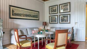 Habitación con sofá, dos sillas de madera, una mesita redonda y una lámpara. Cuatro cuadros enmarcados decoran la pared.