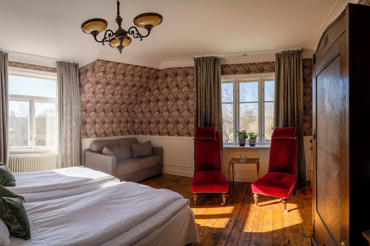 A room with a large bed, two armchairs, a sofa, and a chandelier.