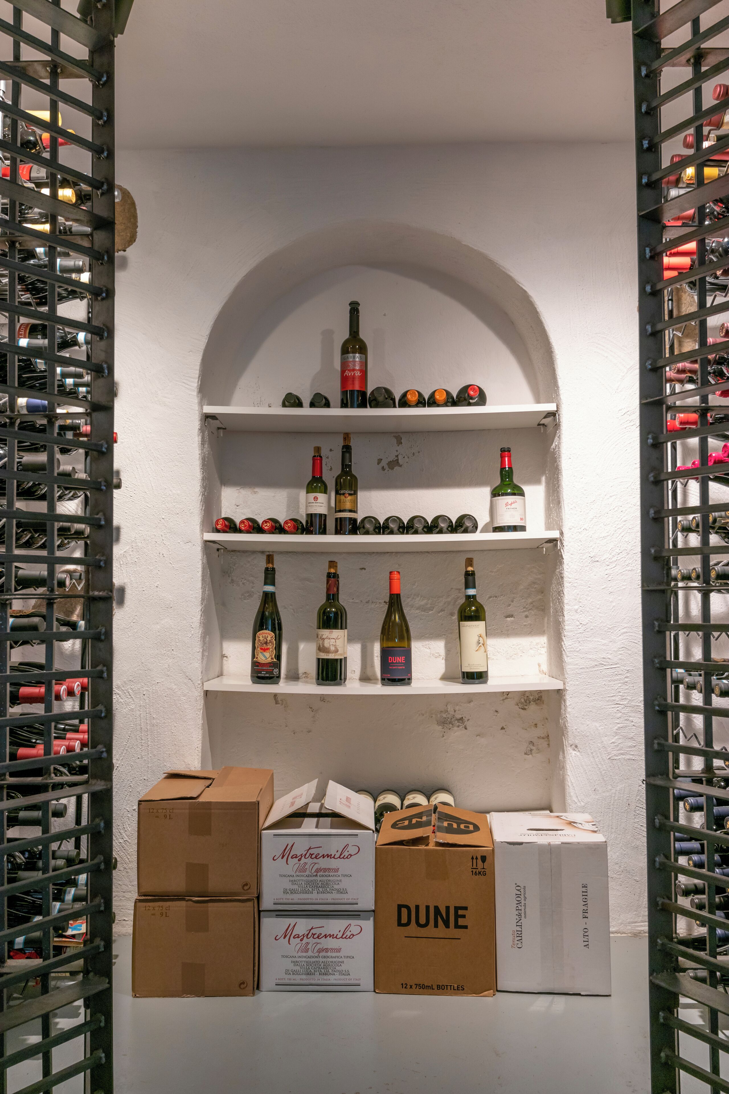 A wine cellar with shelves of wine bottles and boxes labeled 'DUNE' and 'Mestremilio'.