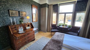 A bedroom with a wooden dresser, a bed, a chair, and a window with a view of the outside. - Villa Gransholm (Gemla)