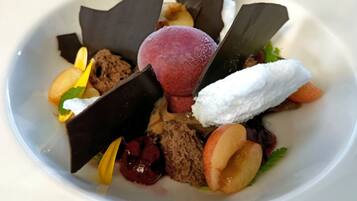 Un plato de postre con diversas frutas, trozos de chocolate y una bola de helado.