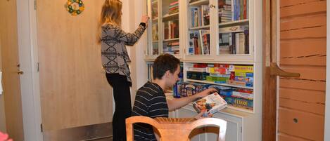 Una habitación con una puerta de madera, una estantería y una persona sentada a una mesa leyendo un libro.