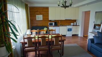 A dining area with a wooden table and chairs, a kitchen with white cabinets, and a blue sofa.