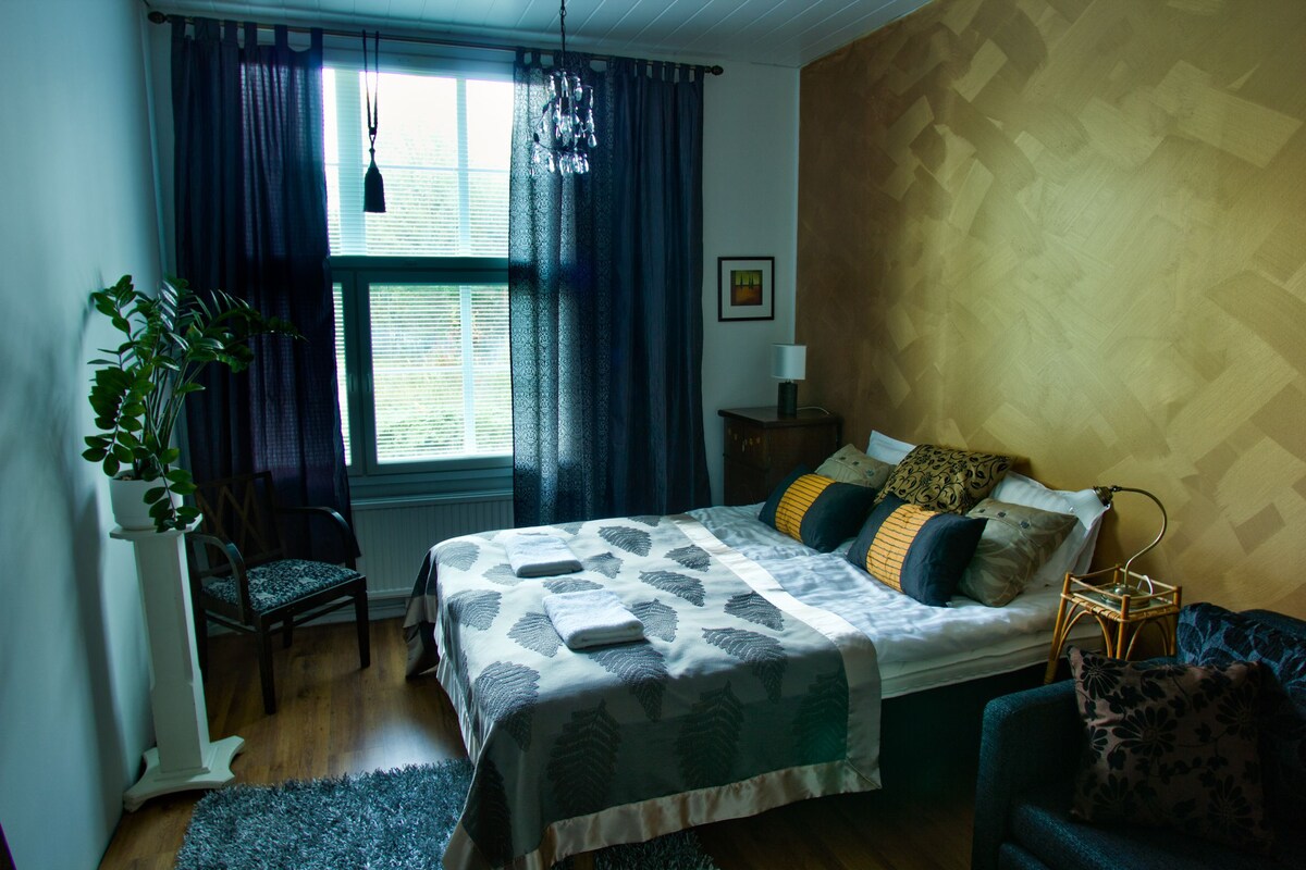 Um quarto com uma cama, uma cadeira, uma planta, uma mesa de cabeceira e um abajur.