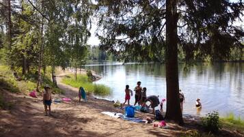 A lakeside campsite with trees, a sandy area, and people engaging in various activities.