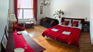 Hotellihuone, jossa on sänky, ruokapöytä tuoleineen, sohva, pieni pöytä lampun kanssa ja ruukkukasvi.