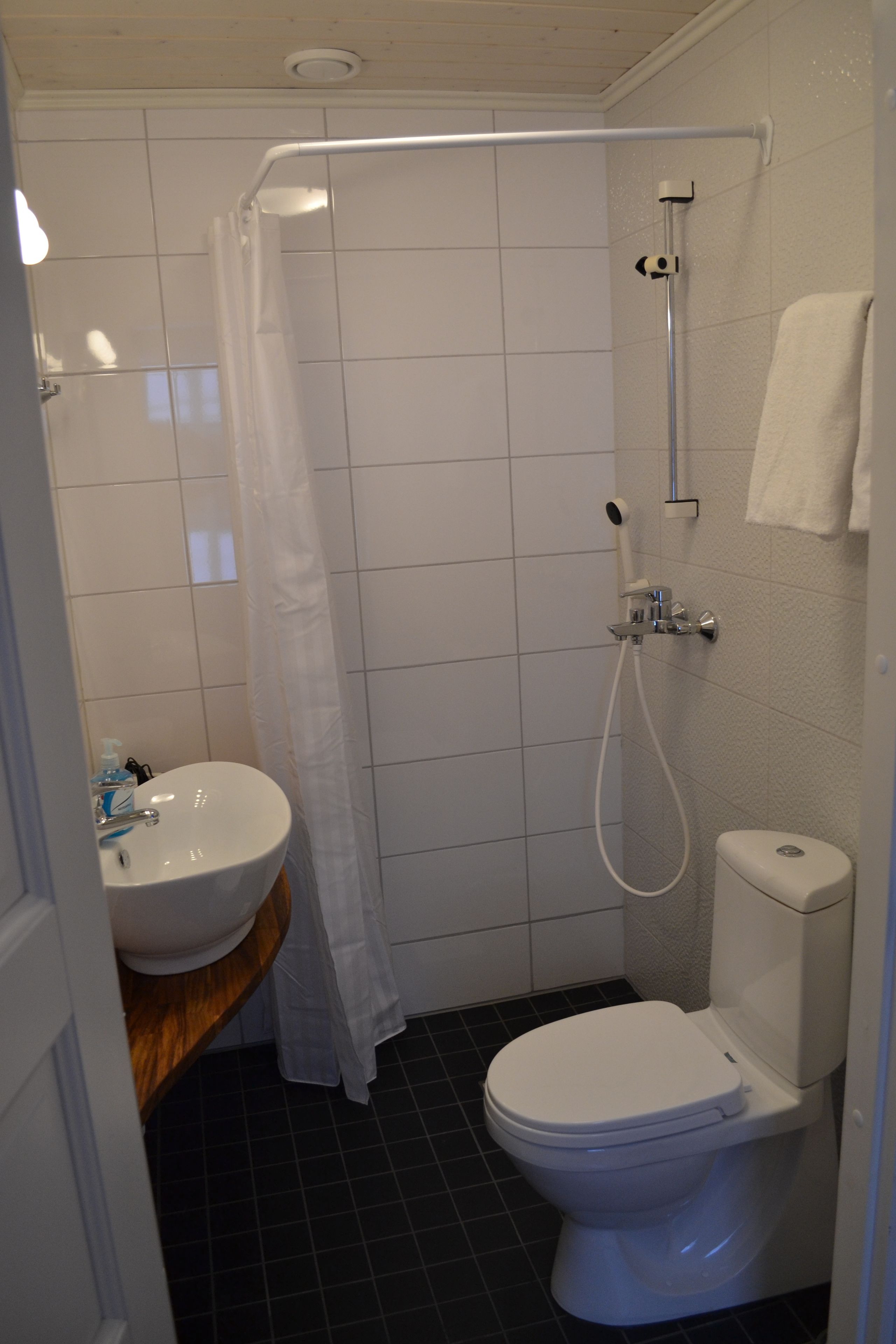 A bathroom with a shower, toilet, sink, and a white towel hanging on the wall.