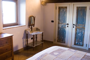 A bedroom with a wooden dresser, a small table with a mirror, a quilt on the bed, and two doors with peeling paint. - Residenza d'epoca & Spa Il Cerchio di Lullo (Fumone)