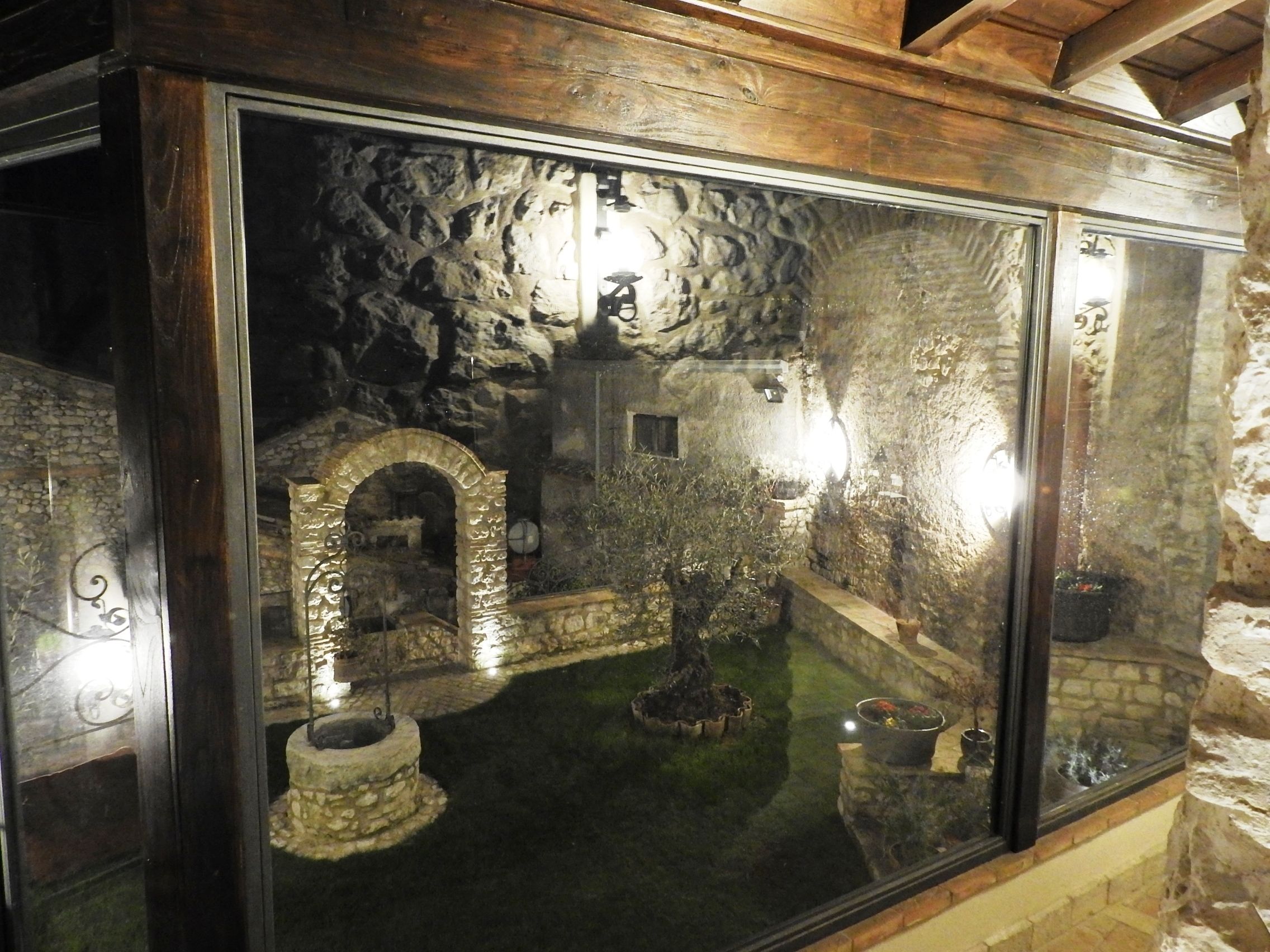 A stone-walled room with a wooden ceiling and a glass window reflecting an interior courtyard.