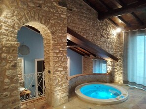 Une pièce aux murs de pierre, dotée d’un jacuzzi, d’un plafond en bois et offrant une vue à travers une arche.