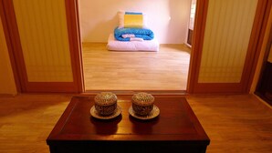 A room with a wooden floor, a small table with two decorative items, and a view of a bed with pillows and a blanket. - HanOK Guest House 201 (Seoul)