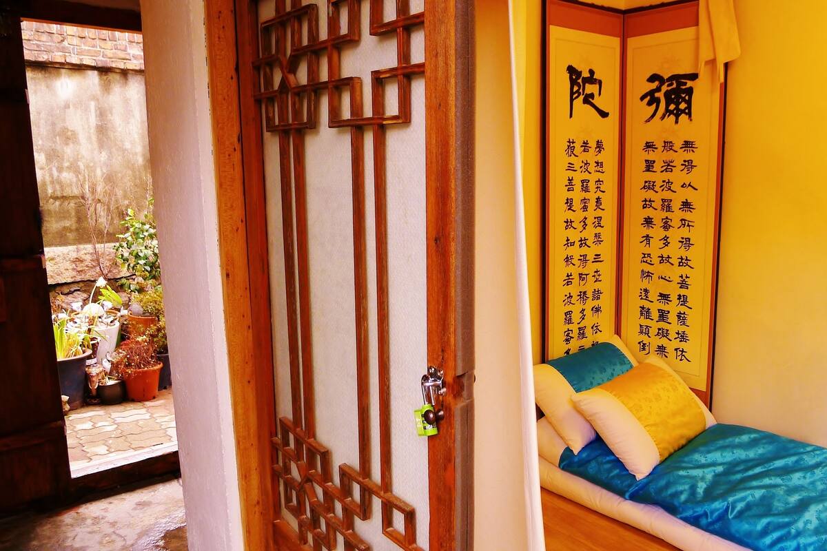 A traditional room with a wooden door, a bed with a blue bedspread, and a wall with Chinese calligraphy.