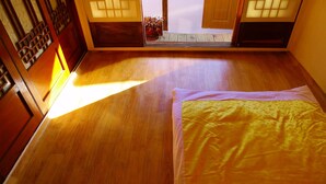 A room with a wooden floor, a bed with a yellow and white bedspread, and a traditional sliding door with a view of the outside. - HanOK Guest House 201 (Seoul)
