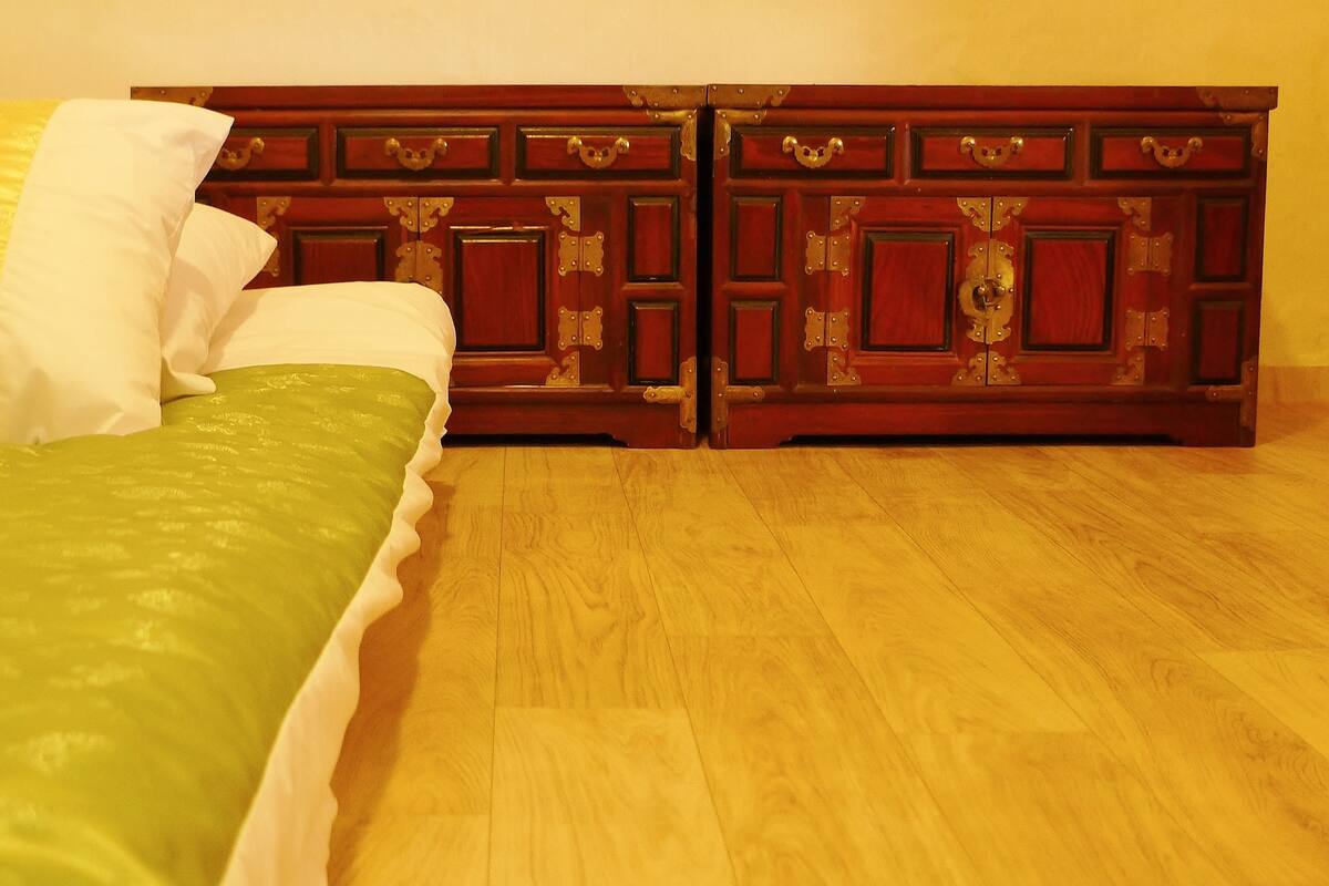 A bed with green bedding and white pillows, a wooden floor, and a wooden wardrobe with metal handles.