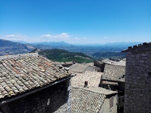 A view of a historic town with stone buildings and terracotta roofs, overlooking a valley and distant mountains. - Locanda Il Falco Nero (Fumone)